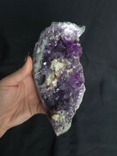 Load image into Gallery viewer, Hand holding a large amethyst crystal against a dark background
