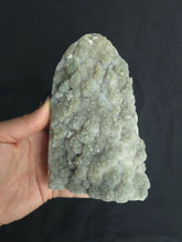 Load image into Gallery viewer, Hand holding a green amethyst freeform rock against a black background
