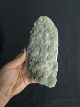 Load image into Gallery viewer, Hand holding a large green amethyst crystal against a black background
