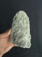 Load image into Gallery viewer, Hand holding a large green amethyst crystal rock against a dark background
