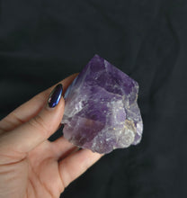 Load image into Gallery viewer, Hand holding a purple crystal against a black background

